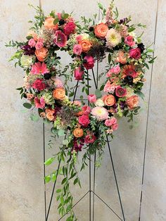 an arrangement of flowers arranged in the shape of a heart on a metal stand against a wall