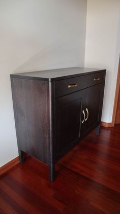 a black cabinet sitting on top of a hard wood floor next to a white wall