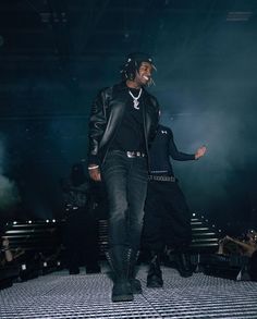 a man walking down a runway wearing headphones and black clothing with people in the background