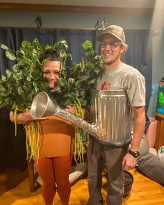 a man and woman dressed up as plants in a living room with a giant metal trash can