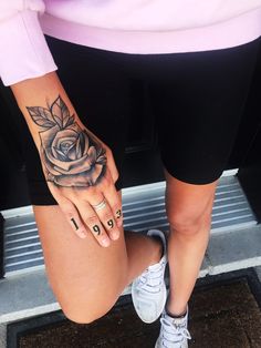 a woman's hand with a rose tattoo on her left arm and the bottom half of her leg