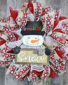 a snowman wreath hanging on the side of a wooden door with red and white ribbons