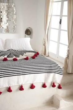 a white bed with red pom poms on it's covers and pillows