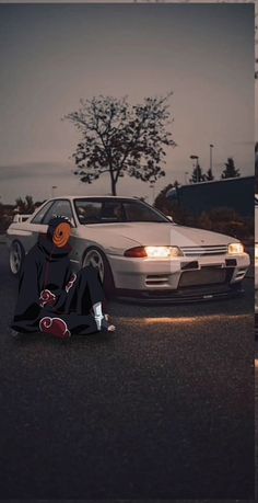 a person sitting on the ground in front of a car with an orange eye patch