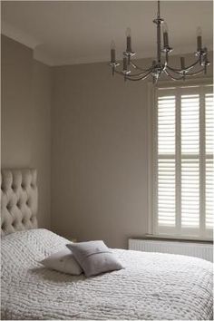 a bedroom with a bed, chandelier and window in the corner that has shutters on both sides