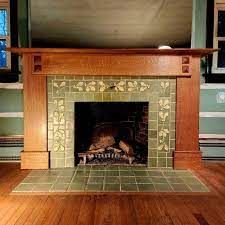 a fireplace in a living room with wood floors and green tile on the mantles