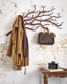 a coat and purse hanging on a white brick wall next to a wooden tree branch