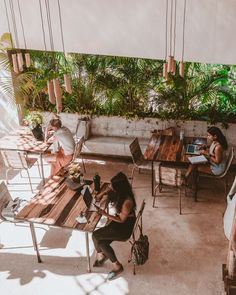 people are sitting at wooden tables in an outdoor cafe with plants on the walls and floor