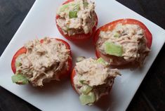 three tomatoes with tuna salad on them sitting on a white platter, ready to be eaten