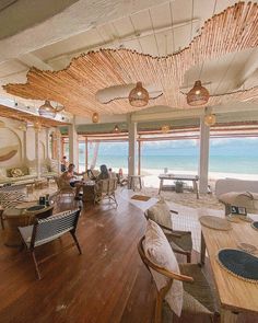 the inside of a restaurant with people sitting at tables and looking out to the ocean