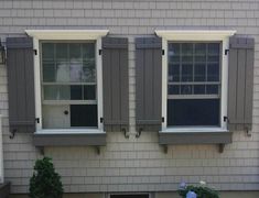 two windows on the side of a house with shutters open and flowers in front