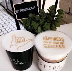 two coffee cups sitting on top of a table next to a potted green plant