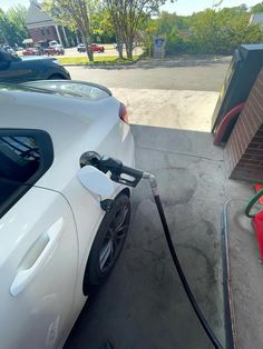 a white car is parked at a gas station with its hose connected to the fuel tank