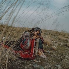 a woman sitting in the middle of a field wearing a red and black outfit with long hair