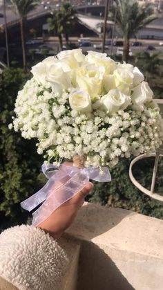 a person holding a bouquet of white flowers on top of a building with palm trees in the background