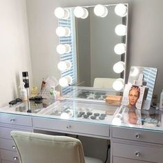 a vanity with a mirror, chair and lights on it in front of a window