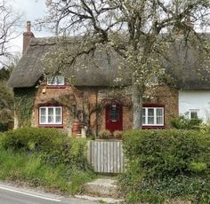 an old brick house with a thatched roof and red shutters on the front