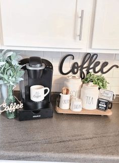 a coffee maker sitting on top of a counter next to two mugs and a potted plant