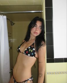 a woman in a bathing suit standing next to a shower stall and looking at the camera