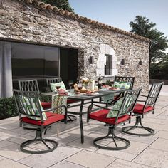 an outdoor dining table and chairs with red cushions on the outside patio next to a stone building