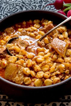 a bowl filled with beans and meat on top of a table next to radishes