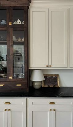 a kitchen with white cabinets and black counter tops, gold trim on the glass doors