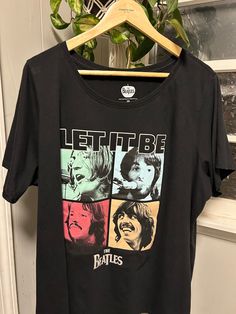 a black t - shirt with the words let it be on it hanging from a wooden hanger