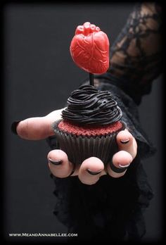 a hand holding a cupcake with a heart on top