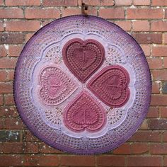 a crocheted doily hanging on a brick wall with hearts in the middle