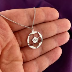 a person holding a silver necklace with the word cru in it's center