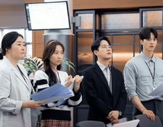 three people standing in front of a tv screen and holding folders with other people behind them