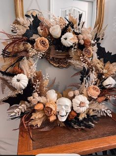 a wreath with flowers and leaves on top of a wooden table in front of a mirror