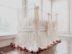 a white crib sitting on top of a hard wood floor next to a window