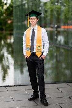 a young man wearing a graduation cap and gown standing in front of a body of water