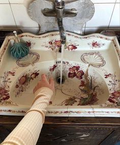 a person washing their hands in a sink with flowers on the bottom and under running faucet