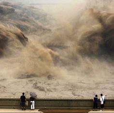 three people standing on a ledge with an umbrella in front of a large amount of sand