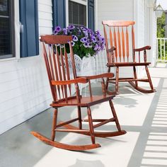 two wooden rocking chairs sitting on a porch with purple flowers in the vases next to them