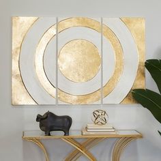 a gold and white art piece sitting on top of a table next to a potted plant