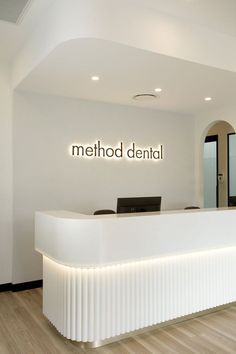 the front desk of a dental office with white walls and wood flooring, along with an illuminated sign that reads method dental