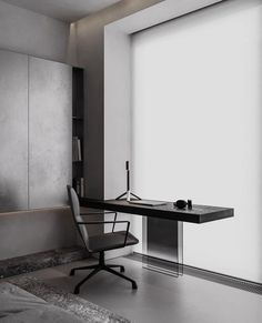 a black and white photo of a desk in a room with large windows, an office chair and a book shelf