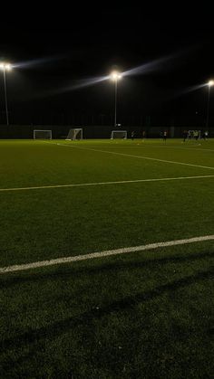 an empty soccer field at night with lights shining on the grass and one goalie waiting for the ball to be thrown