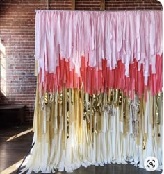 the curtains are lined up with gold, pink and white ribbons hanging from them in front of a brick wall