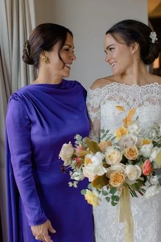 two women standing next to each other in front of a window with flowers on it