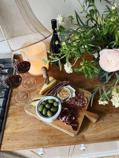 an assortment of food and wine on a wooden cutting board next to a vase with flowers