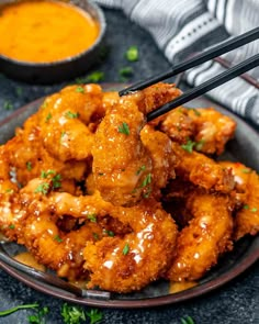 a plate full of chicken wings with chopsticks sticking out of the top and dipping sauce on the side