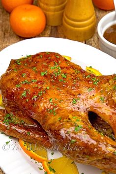 a whole chicken on a white plate with oranges and seasoning next to it