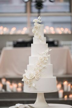 a wedding cake with white flowers on top and candles in the background at a reception