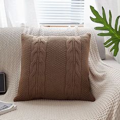 a white couch with a brown cabled pillow on top of it next to a window