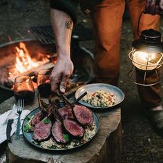 a man is cooking steaks on a grill while another person holds a light over the fire