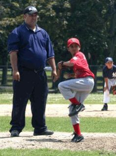 a baseball player pitching a ball on top of a field next to a man in blue shirt and red pants